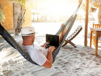 man with hat uses laptop remotely at the beach, near cabin. Playa La Ventanilla